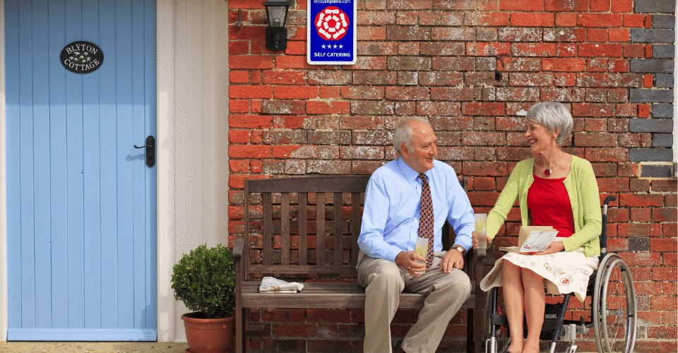 Accessibility Man sitting on bench and woman in wheelchair outside a cottage
